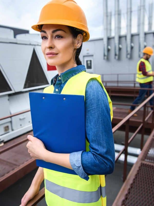 female architect in helmet holding clipboard on roof, male colleague behind